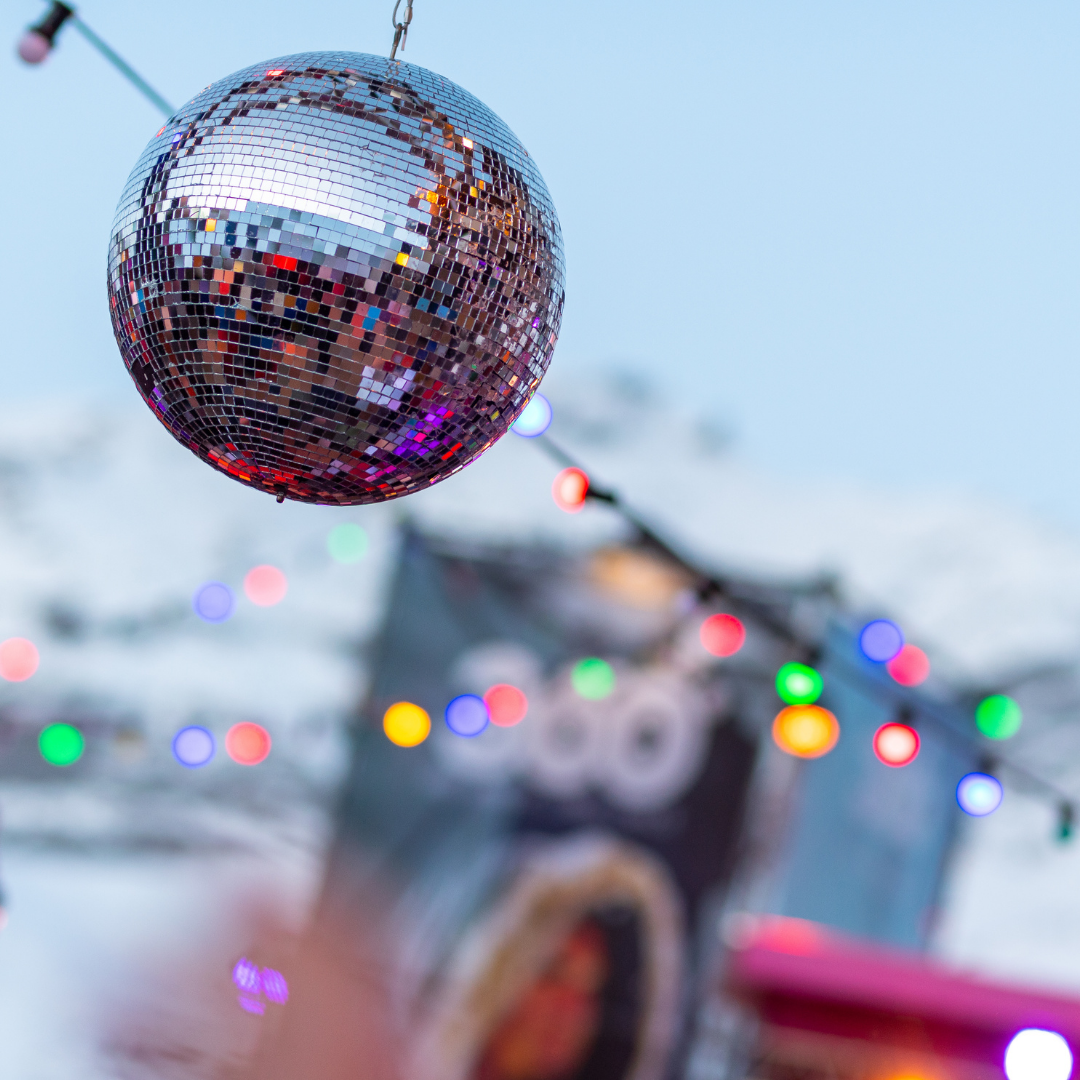 En skinnende discokugle hænger udendørs på baggrund af sløret farverigt lys og en blå himmel, der minder om Nytår på ski-fester, og skaber en festlig atmosfære.