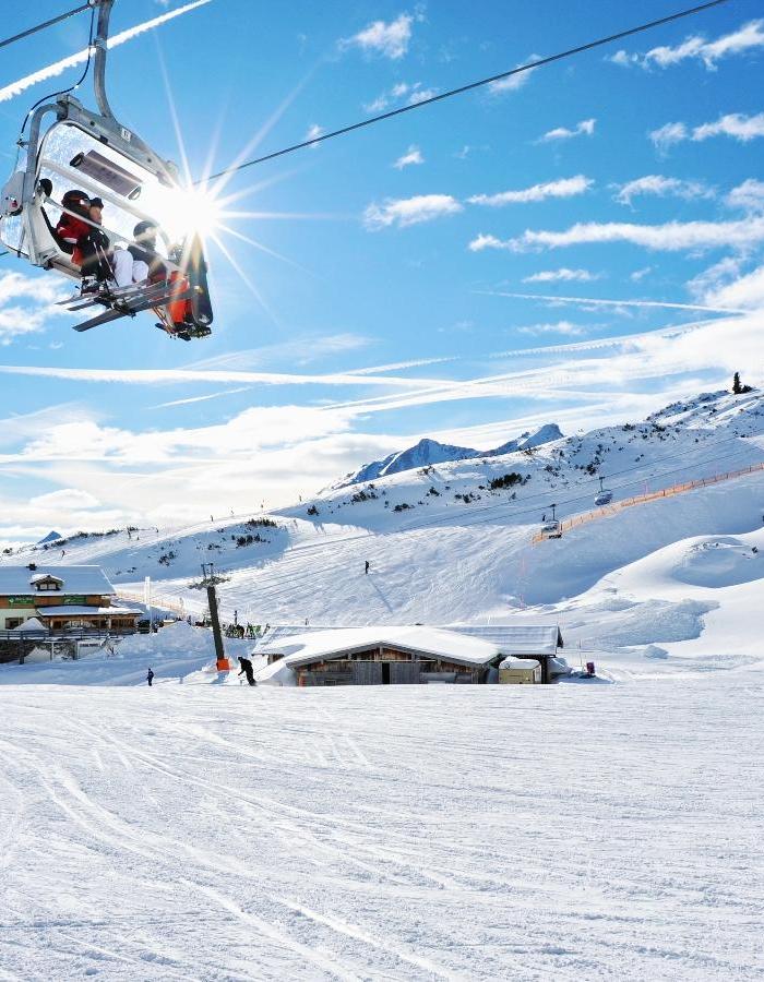 I Wagrains pittoreska snölandskap myllrar ett skidområde av aktivitet. En stollift bär skidåkare graciöst, medan andra glider nerför de orörda backarna. Solljus gnistrar på snön och majestätiska berg reser sig mot en klarblå himmel med spridda moln.