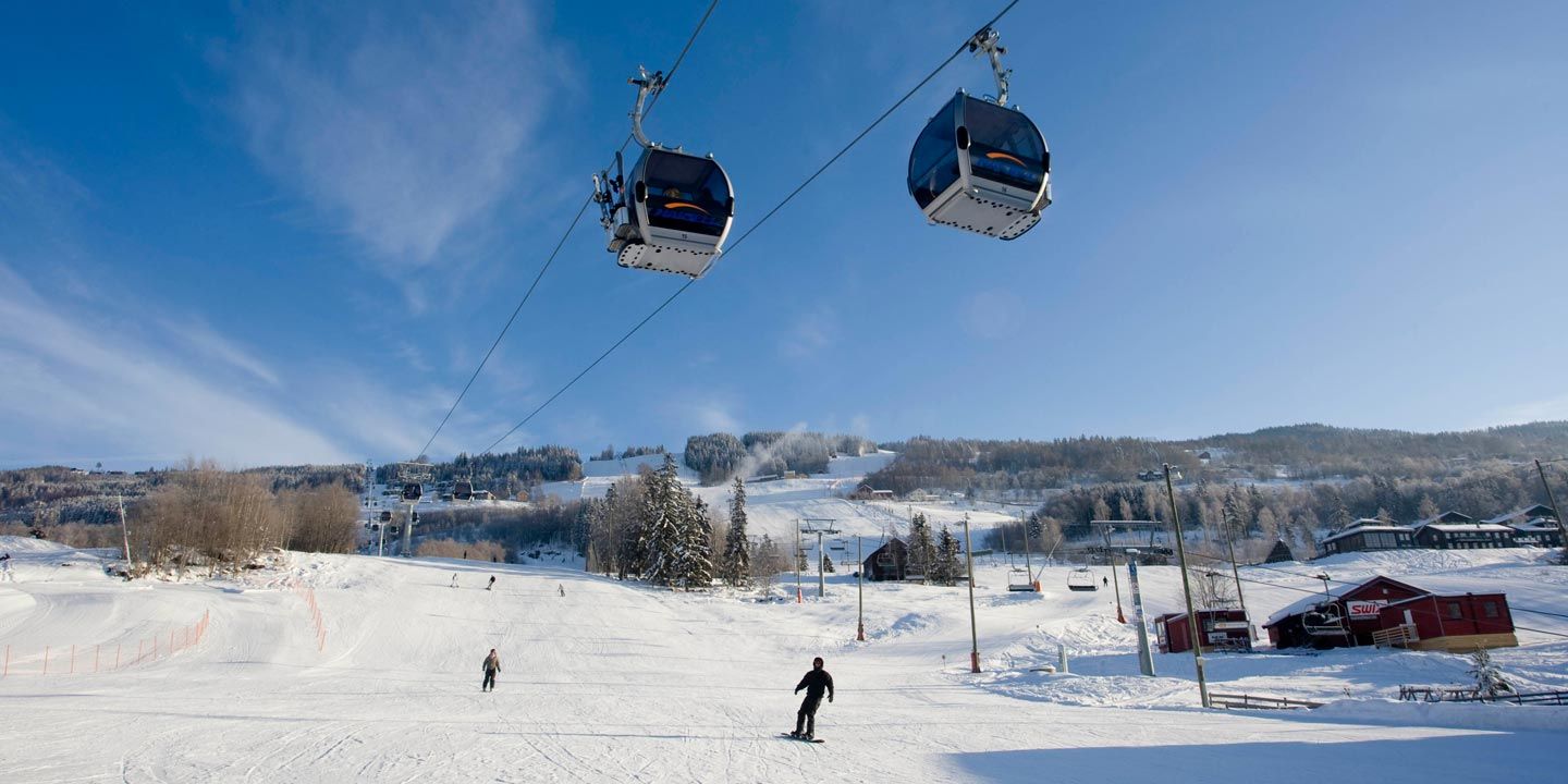 En snöig skidort i Westendorf glittrar under en klarblå himmel. Två gondoler glider över huvudet när skidåkare karar nerför backarna, inramade av charmiga stugor och träd. Scenen fångar den fridfulla tjusningen av en skidferie i Österrikes alpina skönhet.