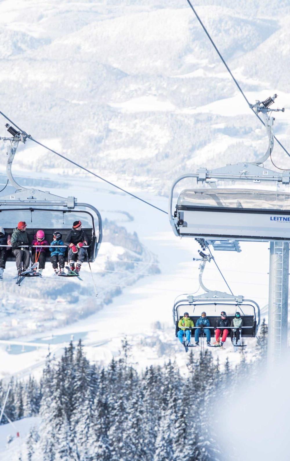 Et skisportssted udfolder sig, mens folk i stolelifte stiger op over Wagrains sneklædte landskab. Træer er støvet med sne, og fjerne bjerge danner baggrunden. Den klare himmel forstærker den vinterlige, fredelige atmosfære, og inviterer skirejseentusiaster til at fordybe sig i dette alpine paradis.