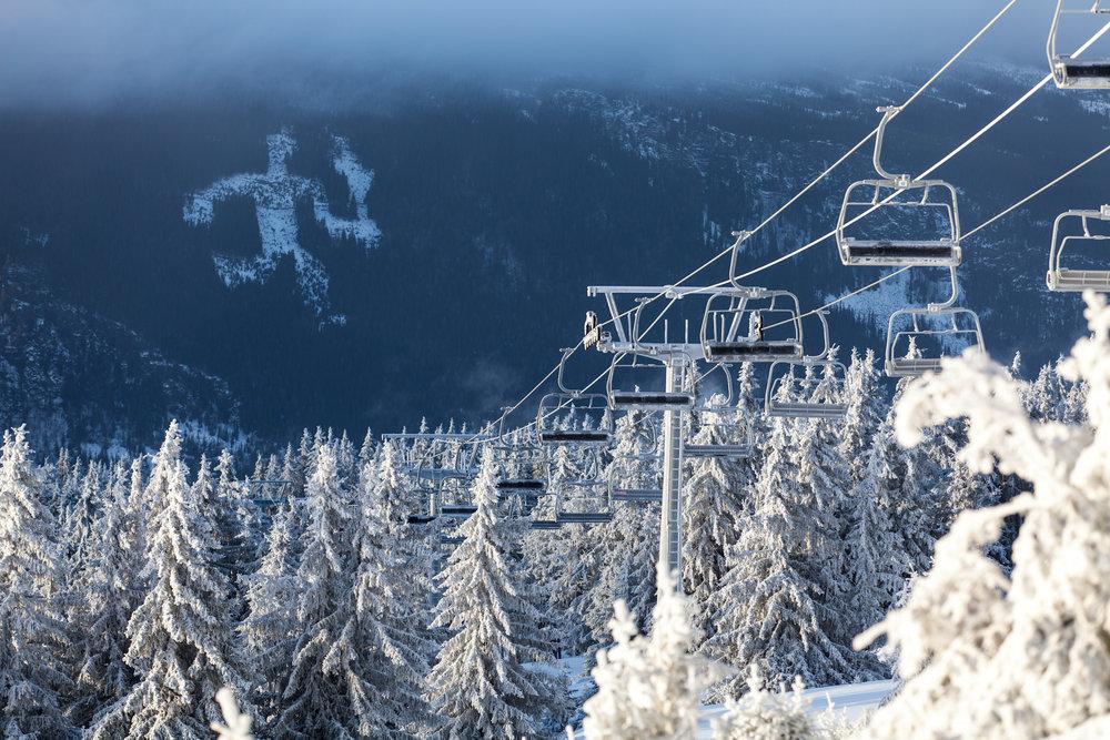 Ett snölandskap med en skidlift med tomma stolar som stiger upp genom en frosttäckt skog i Westendorf. I bakgrunden svävar dimma över en bergskedja under en molnig himmel – en inbjudande scen för dem som drömmer om sin nästa skidsemester.