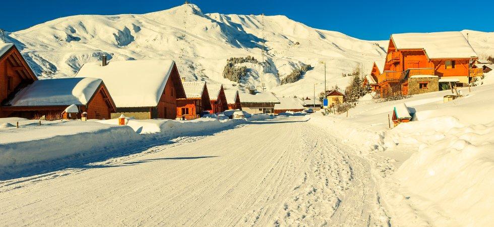 En snöig vinterby med trähus och snötäckta tak ligger vid foten av solbelysta berg under en klarblå himmel - den perfekta miljön för en skiferie i La Toussuire.