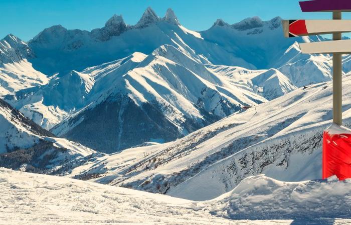 Färgglada skidriktningsskyltar på en snöig bergssluttning under en skiferie i La Toussuire, med panoramautsikt, snötäckta toppar och klarblå himmel i bakgrunden. Skyltens bas är inslagen i ljusrött material.