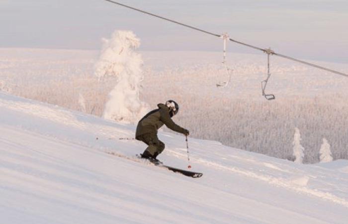 En person i vinterkläder åker skidor nerför en snöig backe under en skidlift i Sälen, med snötäckta träd och en blek himmel som inramar deras perfekta skiferie i Sälen.