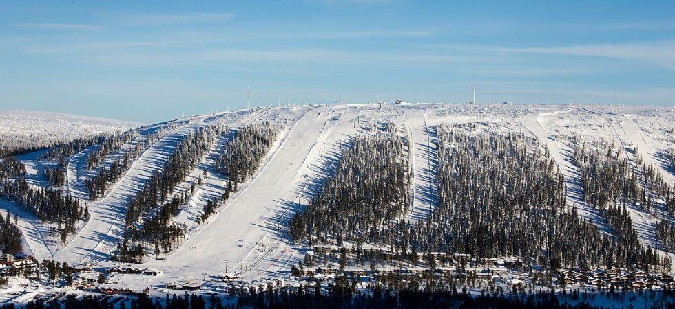 En snötäckt skidort med flera skidbackar, perfekt för en skiferie i Sälen, omgiven av träd och mysiga stugor vid foten av berget under en klarblå himmel.