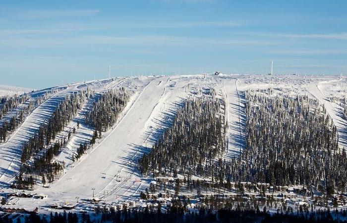 En snötäckt skidort med flera skidbackar, perfekt för en skiferie i Sälen, omgiven av träd och mysiga stugor vid foten av berget under en klarblå himmel.