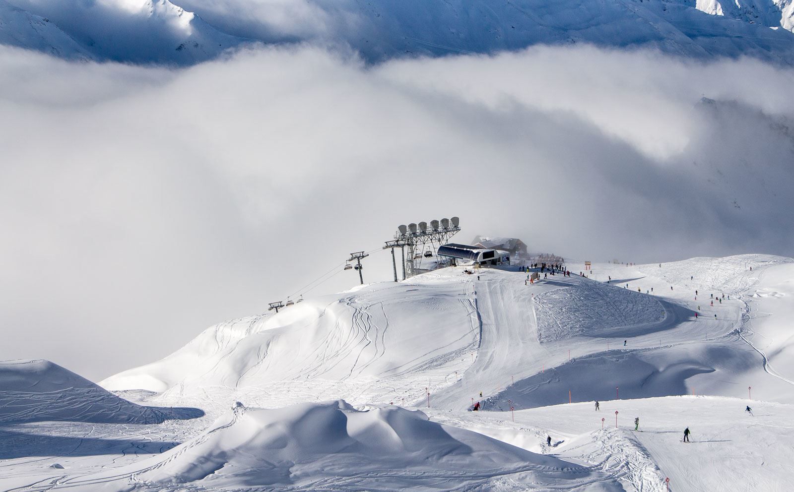 En snötäckt skidort i Saalbach med skidliftar, en skidstation och skidåkare utspridda i backarna, omgivna av berg och lågt hängande moln – en idealisk plats för din nästa skidresa eller spännande skidresa.
