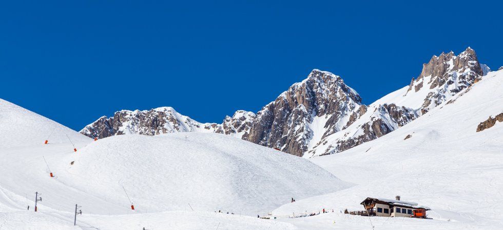 Snötäckta berg under en klarblå himmel, med en skidstuga och skidliftar synliga i förgrunden. Detta natursköna vinterlandskap fångar perfekt essensen av en skiferie i Tignes bland majestätiska klipptoppar.