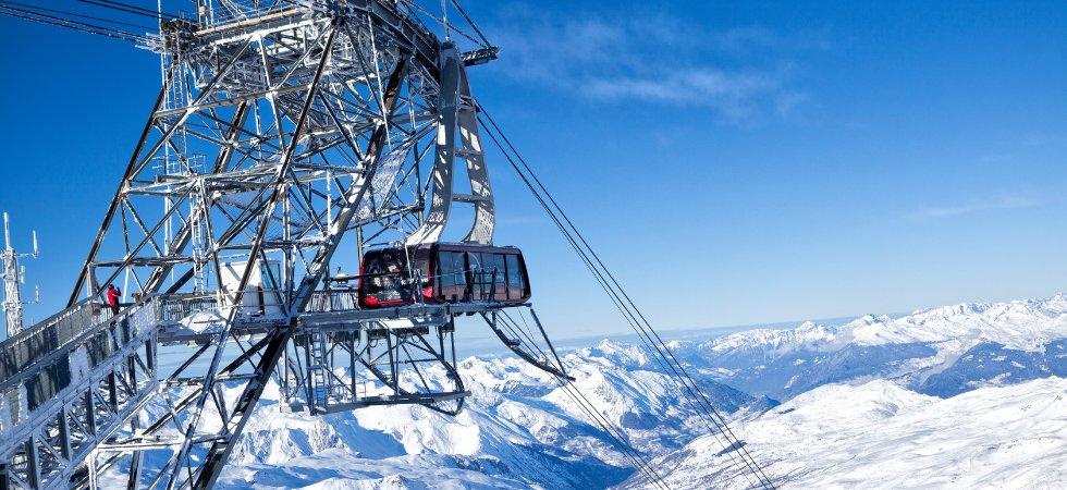 En svævebane afgår fra en metalstation højt i de sneklædte bjerge under en skiferie. Himlen er klar og blå og tilbyder panoramaudsigt over de omkringliggende snedækkede tinder og dale. Nogle få mennesker står på platformen i Wagrain og observerer det betagende landskab.