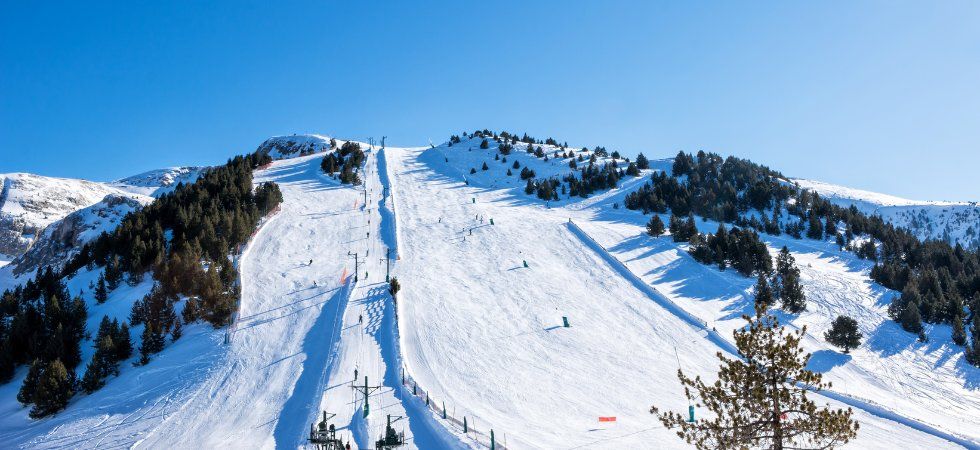 En snötäckt skidbacke en solig dag, med skidåkare som använder en skidlift och spridda pinjeträd längs bergssidan under en klarblå himmel - perfekt för en skiferie i Val Thorens.
