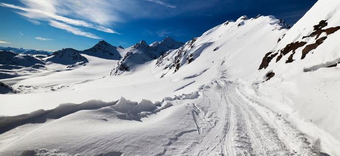 Snötäckt bergslandskap med karga toppar under en blå himmel, med en slingrande stig i förgrunden - perfekt för ett oförglömligt äventyr med skiferie i Val Thorens.