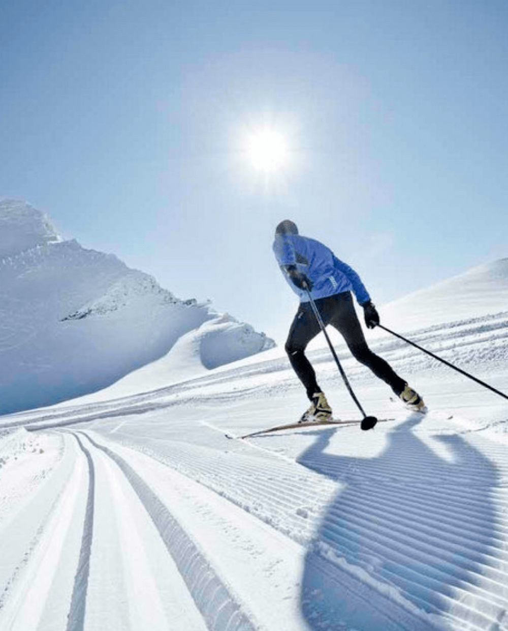 En person i vinterkläder åker längdskidor på ett preparerat snöigt spår i Wagrains ljusa, soliga berg. Himlen är klar och solen skiner ovanför, vilket skapar en perfekt dag för skidåkarentusiaster.