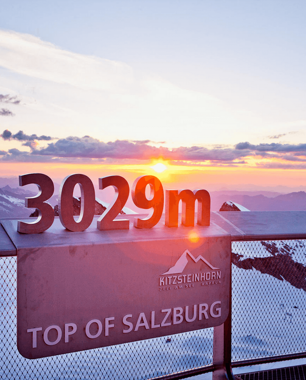 Oplev den betagende udsigt over solopgangen fra Kitzsteinhorn-gletsjeren på toppen af Salzburg, Østrig. På 3029m er snedækkede bjerge og skyer badet i solens varme skær – en perfekt start på dit skiferieeventyr, kun en kort rejse fra Wagrain.