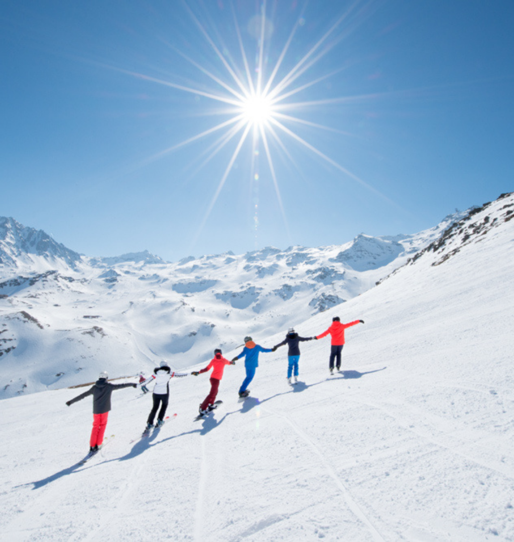 En gruppe på fem personer nyder Nytår på ski og står på ski ned ad en sneklædt bjergskråning under en skarp, skinnende
