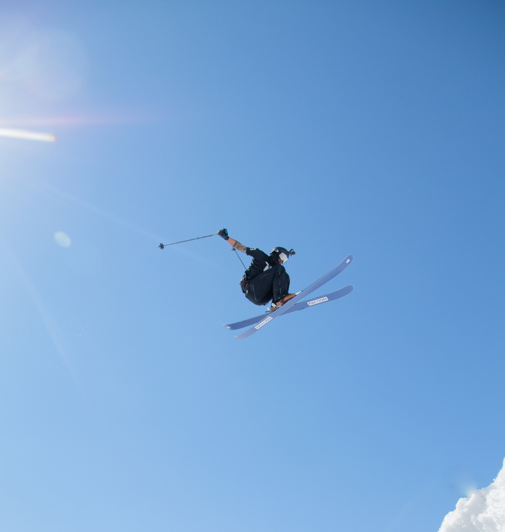 En skiløber fejrer Nytår på ski med et højtflyvende trick mod en klar blå himmel. Solen kaster et skarpt skær øverst